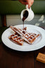 Gaufres dorées saupoudrées de sucre glace avec sauce chocolat versée d'une tasse blanche Verlet